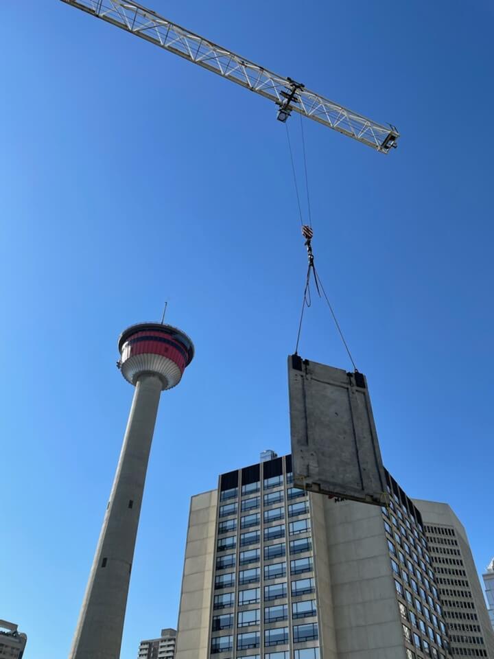 A crane lifts one of the original concrete exterior panels off the building