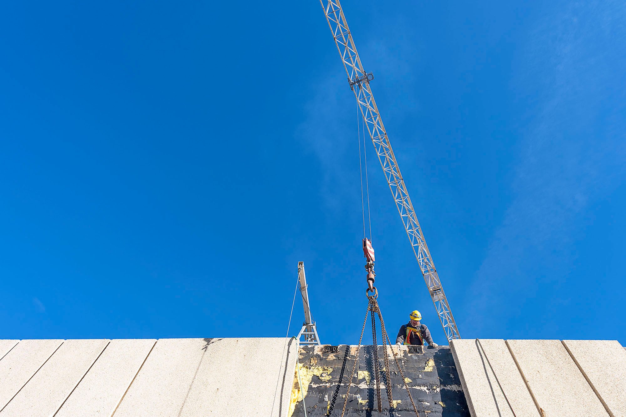 Person in hardhat looks at black insulation, with bright sky overheard