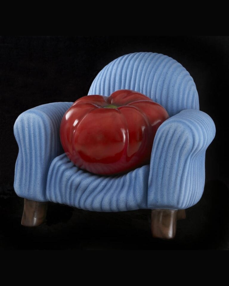 A large ceramic tomato sits upon a blue ceramic chair.