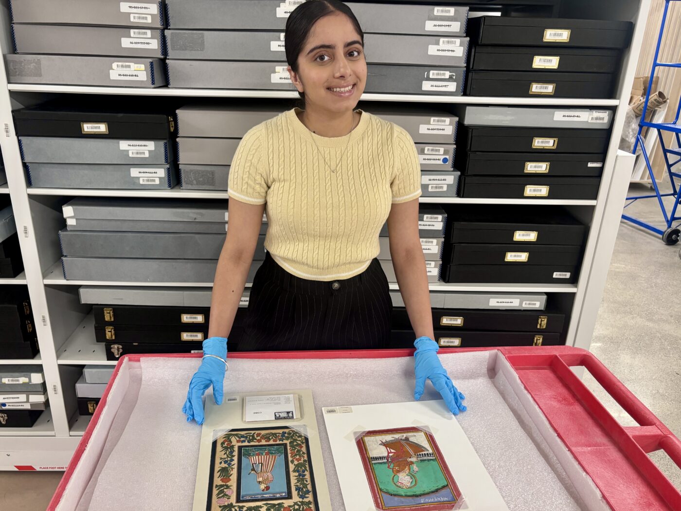 A woman stands over two paintings on a table.