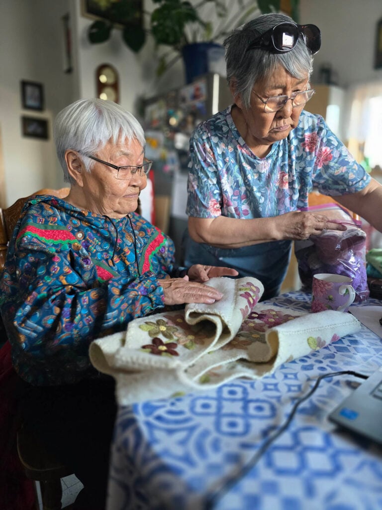 Two older women look at embroidered fabric