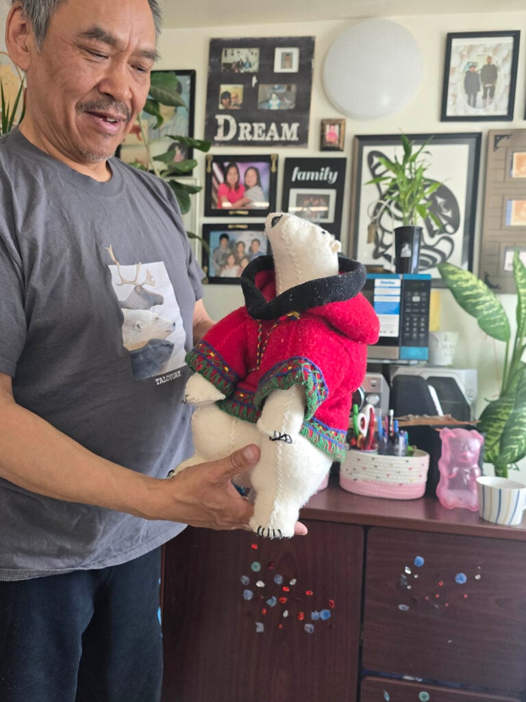 A man holds a packing doll - a plush polar bear, about the size of two hands, wearing a warm coloured coat
