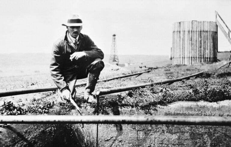 Black and white photo of a man standing by an oil well.