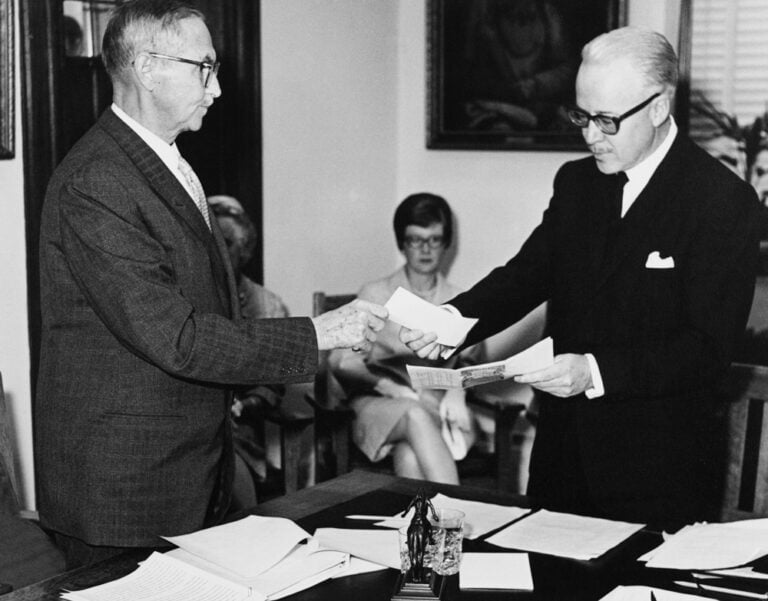 A black and white photo of a man handing a cheque to another man.