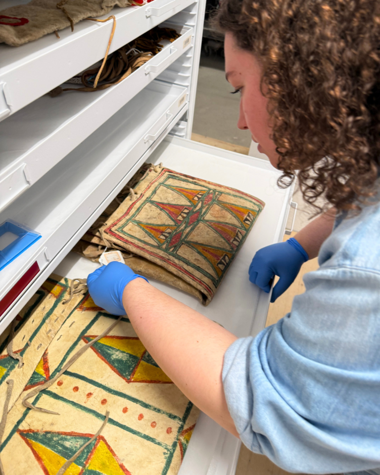 A woman observes flat rawhide containers painted with geometric designs.