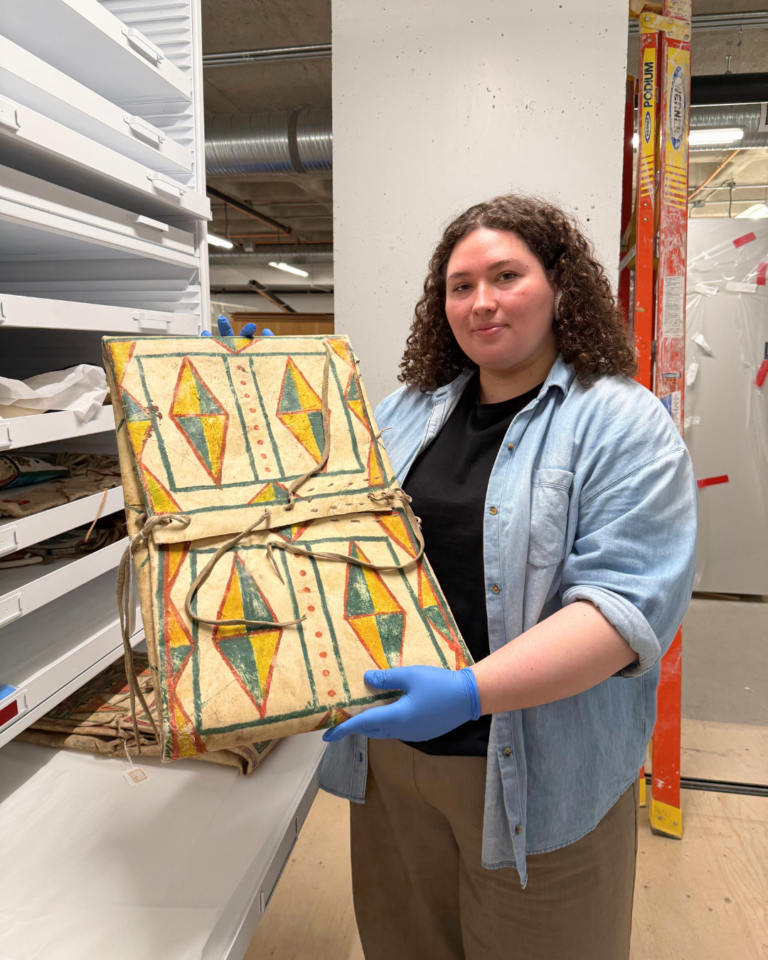 A woman holds a flat rawhide container painted with a green and yellow geometric design.