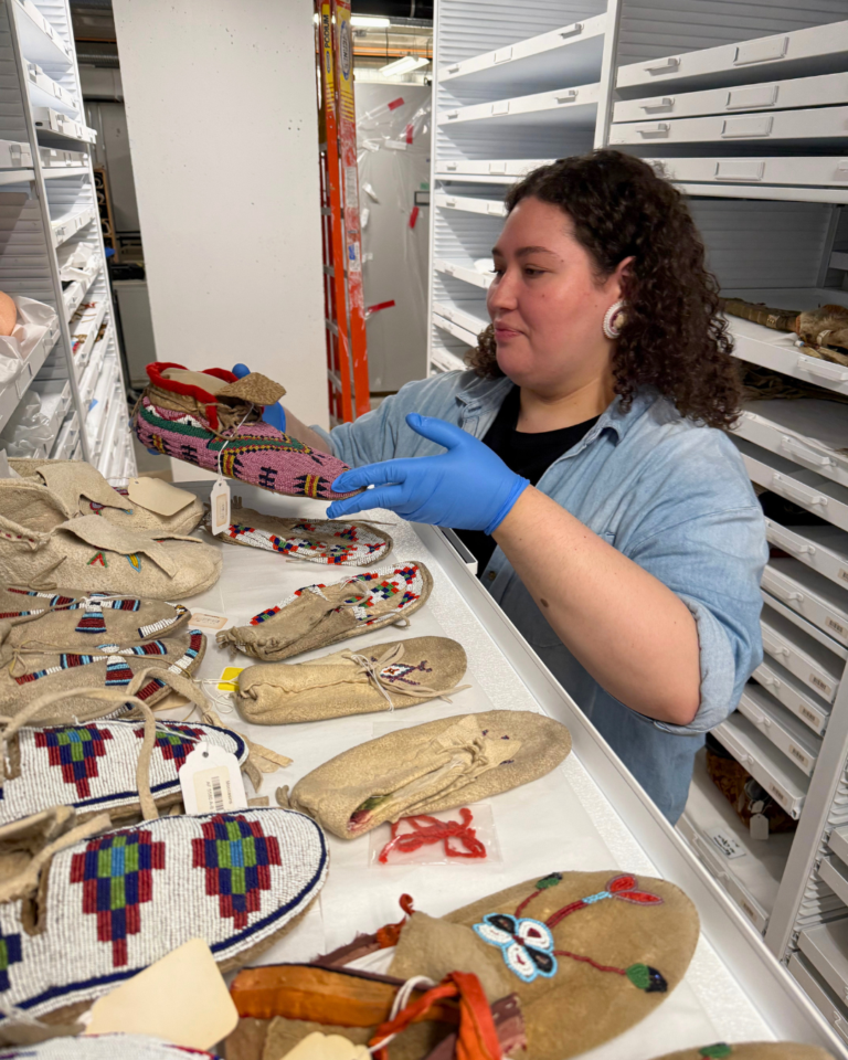 A woman holds a pink beaded moccasin in museum storage.
