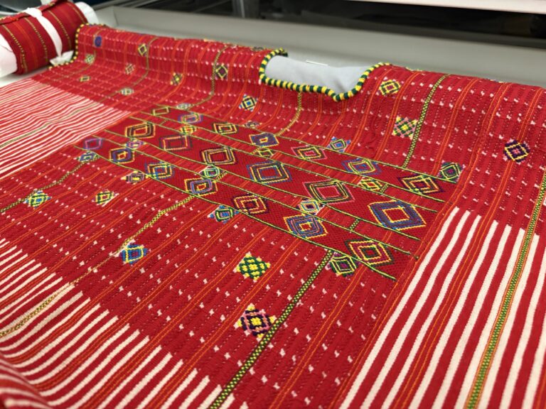 A red woven garment decorated with multicoloured, geometric shapes.