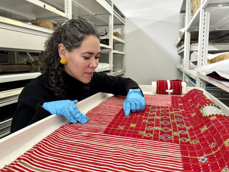 A woman observes a red woven textile in museum storage.