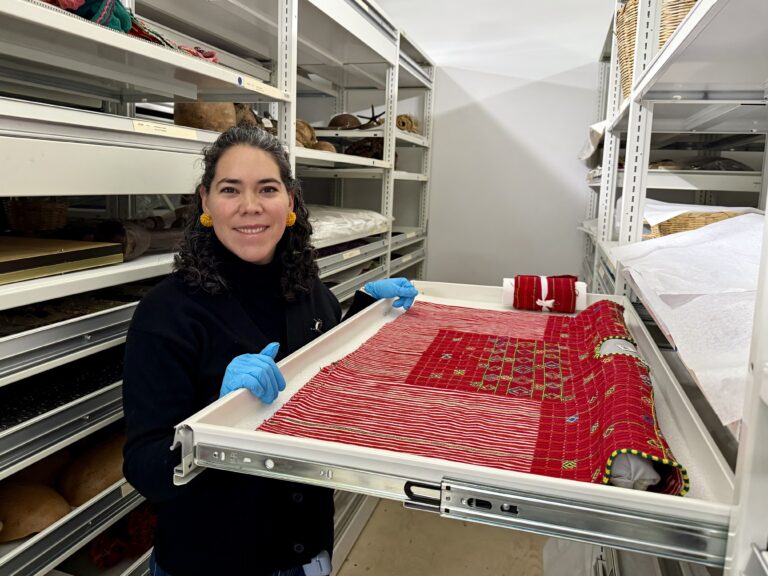 A woman observes a red woven textile in museum storage.