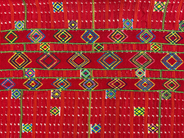 A red woven garment decorated with multicoloured, geometric shapes.
